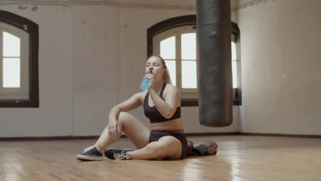 Long-shot-of-woman-drinking-water-after-boxing-workout-in-gym